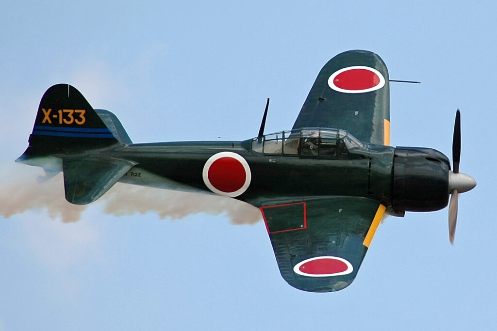 An A6M3 Zero replica in flight witht smoke coming from the engine.