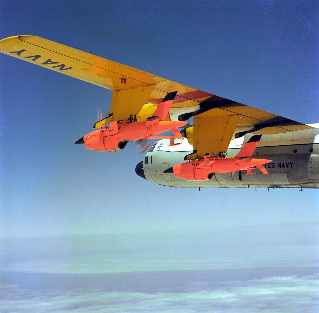 An air-to-air left side view of a DC-130 Hercules drone control aircraft carrying two BQM-34S Firebee target drones under its wing.  The aircraft is assigned to Fleet Composite Squadron 3 (VC-3).